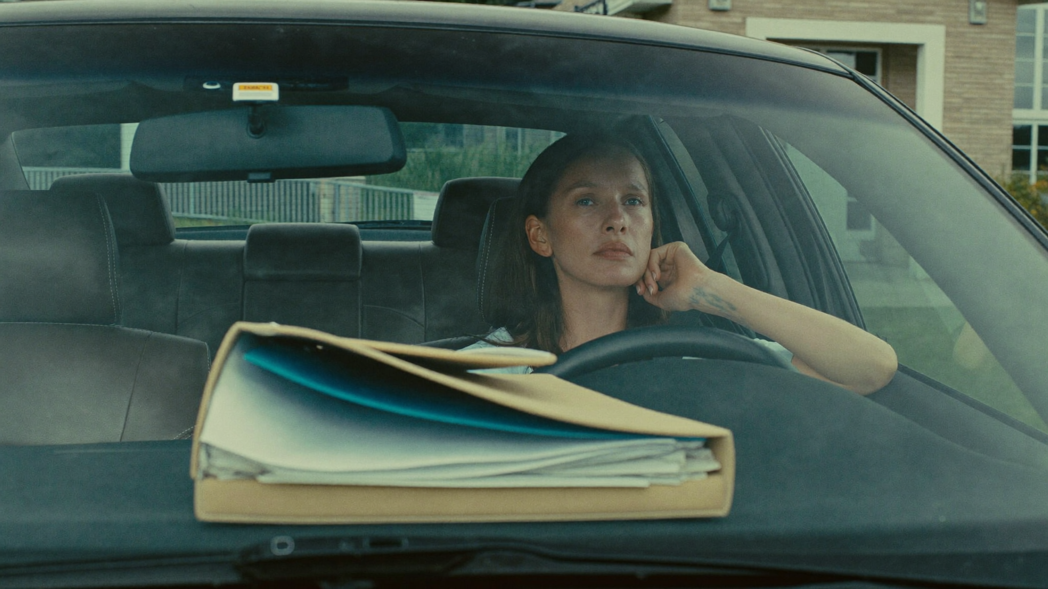 Woman sitting in her parked car outside a medical office, hand at her throat, folder of test results on the seat